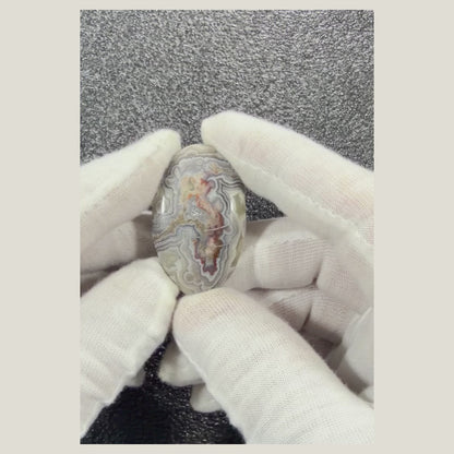 Close-up video of a one-of-a-kind Crazy Lace Agate cabochon displaying natural cream, tan, gray, and golden banding from multiple angles.